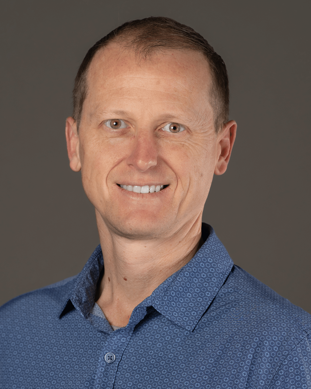 a man wearing a blue shirt and smiling at the camera